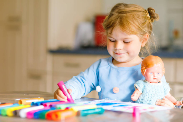 little alone toddler girl painting with felt pens during pandemic coronavirus quarantine disease. Happy creative child with old vintage doll, homeschooling and home daycare with parents - Photo, Image