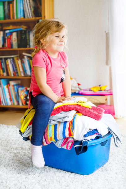 Little girl with a big basket of fresh clean laundry ready for ironing. Happy beautiful toddler and baby daughter helping mother with housework and clothes. - Foto, immagini