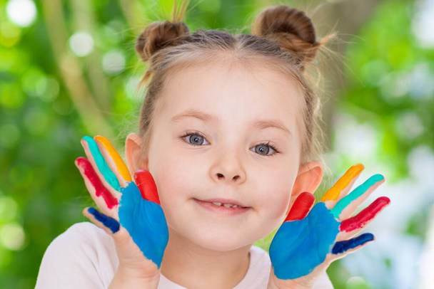 Una niña con las palmas manchadas de pintura. Emociones de una infancia feliz y creatividad
. - Foto, Imagen