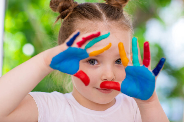 Een klein meisje met haar handpalmen gekleurd in verf. Emoties van een gelukkige jeugd en creativiteit. - Foto, afbeelding