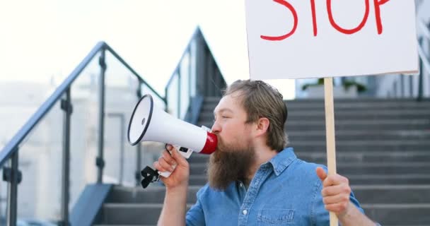 Close up of Caucasian male activist with beard screaming in megaphone speaker. Man holding poster Stop at political or environmental lonely demonstration. Single protest outdoor. Activism work. - 映像、動画