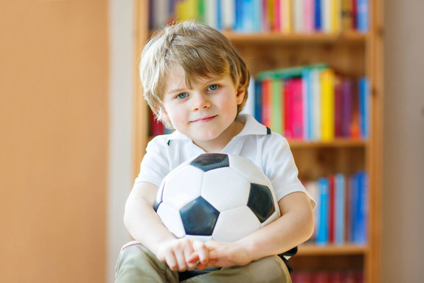 Little blond preschool kid boy with ball watching soccer football cup game on tv. Funny happy crying child fan having fun and cheering winning football team. Champions and world cup concept - Foto, Imagem