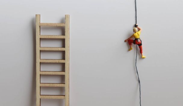 Una donna in miniatura sale una corda accanto a una scala di legno
. - Foto, immagini