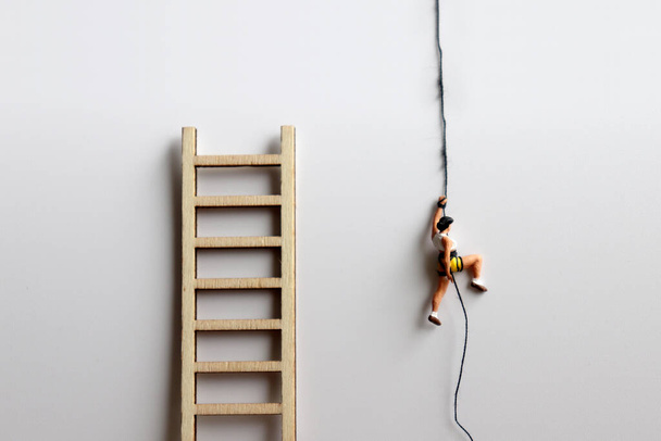  Миниатюрная женщина взбирается по веревке рядом с деревянной лестницей
. - Фото, изображение