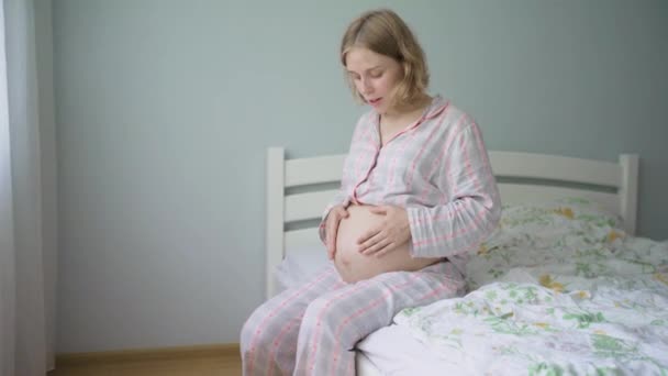 Zwangere vrouw oefent ademhalingstechniek tijdens het zitten op het bed thuis. - Video
