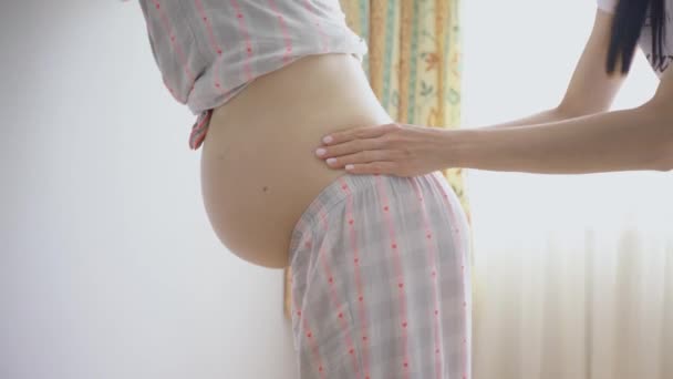 Een zwangere vrouw wordt gewreven en gemasseerd haar rug is om de pijn van de zwangerschap te verlichten. - Video