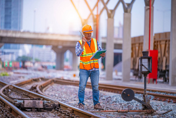 Engineer under inspection and checking construction process railway switch and checking work on railroad station .Engineer wearing safety uniform and safety helmet in work. - Photo, Image