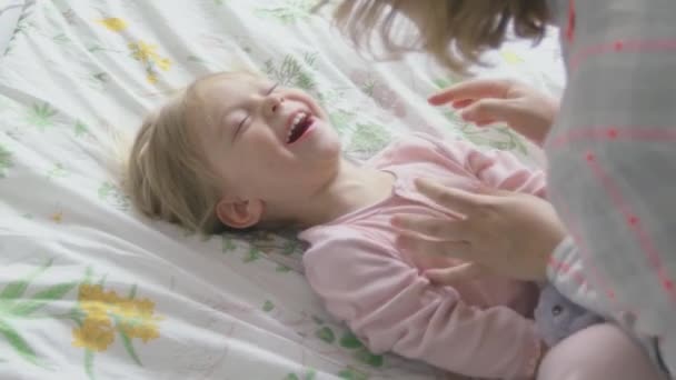 Close-up. Mom tickles little daughter in bed. The family has fun at home. - Imágenes, Vídeo