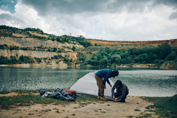 Two handsome men disassembling tent. Camping at weekend concept. - Фото, зображення