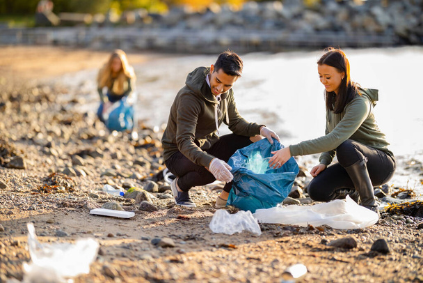 Equipo de voluntarios dedicados y sonrientes recogiendo basura en la playa
 - Foto, Imagen