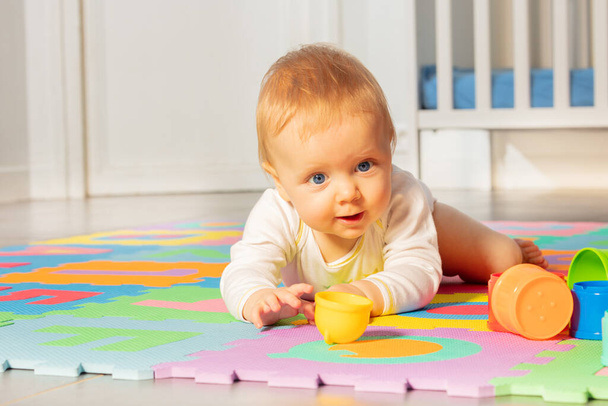 Beautiful baby toddler boy, lay and crawl in front of crib play reaching toys on the carpet - Foto, Bild