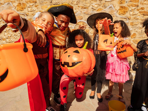 Many kids in Halloween costumes stand together holding pumpkin in a group of friends with buckets for candies - Photo, Image