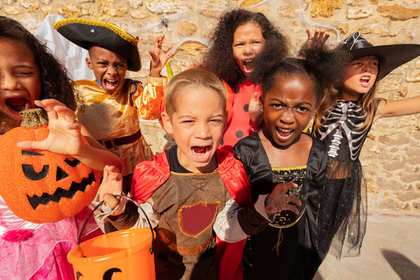 Many kids scream and look at camera in Halloween costumes standing together in a group of friends - Foto, Imagem
