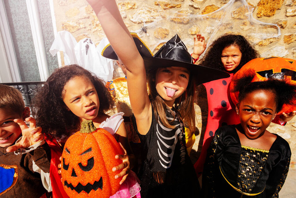 Cute girl sticking out tongue in Halloween costume playing and making fun, holding pumpkins in a group of friends - Foto, Imagen