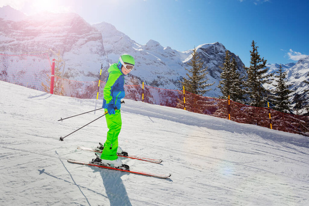 Cute 10 years old boy skier racing fast down the slope in bright green ski outfit on sunny day - Foto, Bild
