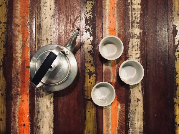 Чайник и три чашки на деревянном фоне стола, вид сверху
 - Фото, изображение