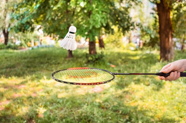 Racket with a shuttlecock in the air on a background of greenery. Playing badminton in the open air - Фото, изображение