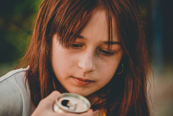 Een jong meisje drinkt water. Tiener meisje drinkt met een ijzeren blik. Een 9-jarig meisje houdt een drankje in haar handen. Tiener meisje 9 of 10 jaar oud met bruin haar. - Foto, afbeelding