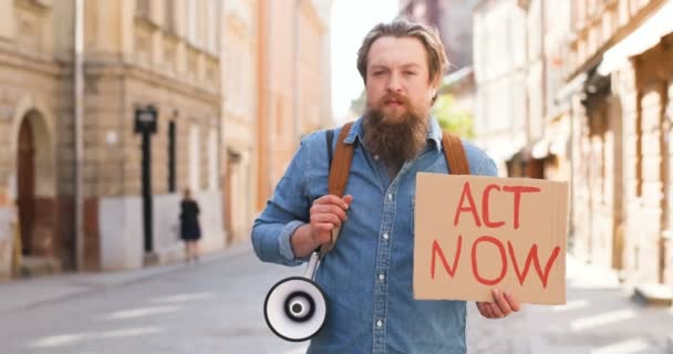 Портрет кавказького чоловічого активіста з бородою, що тримає в руках плакат тепер і мегафон на політичній або екологічній самотності в місті. Одинокий протест. Людина протестує сама. - Кадри, відео