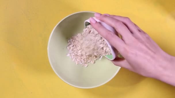Les mains féminines versent de la farine d'avoine dans une assiette verte et versent le yogourt d'une bouteille blanche. Des images FullHD de haute qualité - Séquence, vidéo