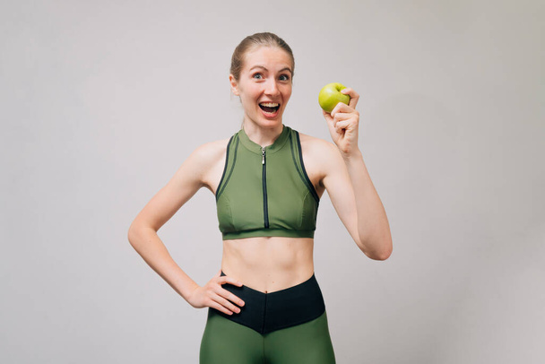 Urheilullinen hoikka tyttö, jolla on vihreä omena käsissään. Fitness malli lyhyt teema ja leggingsit. Onnellisuus käsite hymy laihtumiseen nuori nainen. - Valokuva, kuva