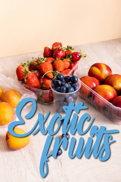 blueberries, strawberries, nectarines and peaches in plastic containers near exotic fruits lettering on beige - Photo, Image