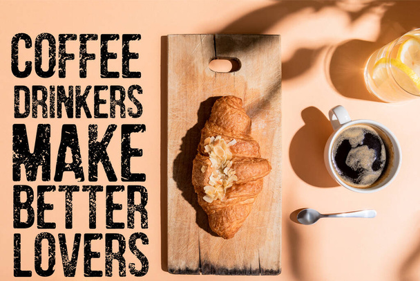 top view of coffee, water and croissant on wooden board for breakfast on beige table with coffee drinkers make better lovers lettering  - Foto, Bild