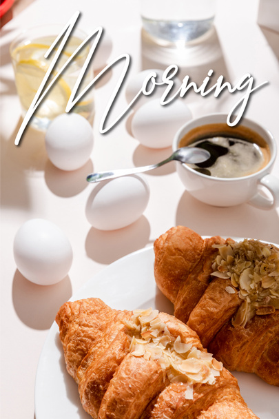 Főtt tojás, két croissant, egy csésze kávé és egy pohár víz citrommal reggelire szürke asztalon, reggeli felirattal.  - Fotó, kép