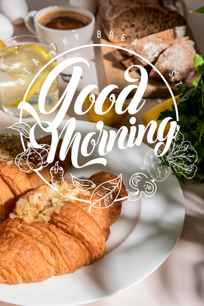cruasanes frescos, pan, café y agua de limón en la mesa gris, enfoque selectivo con desayuno saludable, letras de buenos días
 - Foto, Imagen