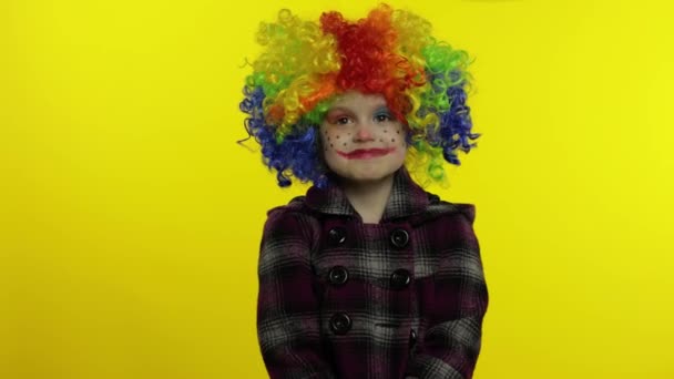 Kleines Kindermädchen Clown mit bunter Perücke macht alberne Gesichter, sieht mit Augen in verschiedene Richtungen - Filmmaterial, Video