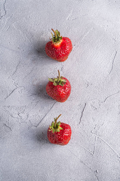 Свіжі стиглі полуничні фрукти в ряд, літні вітамінні ягоди на сірому кам'яному фоні, вид зверху
 - Фото, зображення