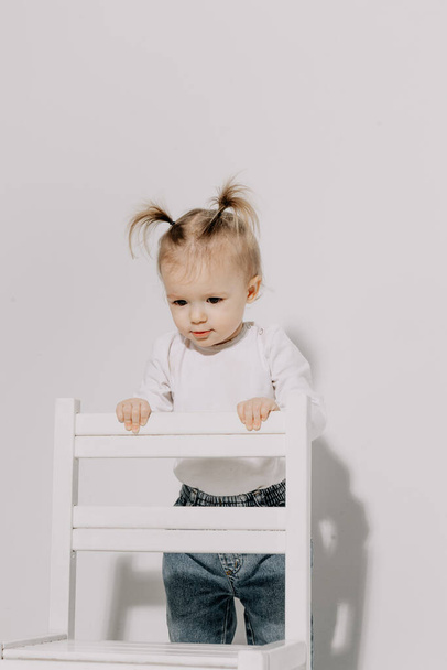 cute little girl with a ponytail hairstyle dressed in a white T-shirt and denim pants posing for a photo on a white background in a photo studio - 写真・画像