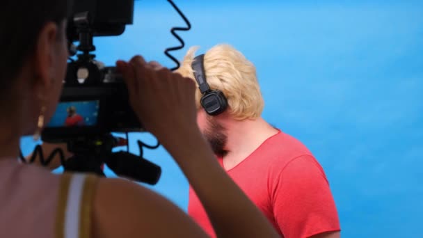freaky dikke man in een pruik en een roze t-shirt maakt een video blog tegen een blauwe achtergrond. - Video