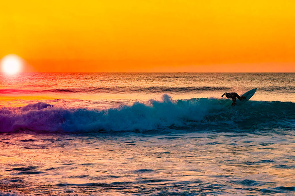 The silhouette of a surfer riding a wave at an empty surf spot. Young surfer rides the wave during sunset. Image - Photo, Image