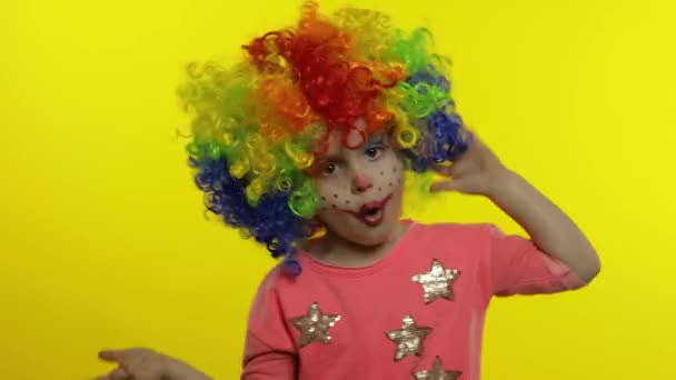Kleines Kindermädchen Clown mit Perücke macht dumme Gesichter. Spaß haben, lächeln, Zunge zeigen. Halloween - Filmmaterial, Video