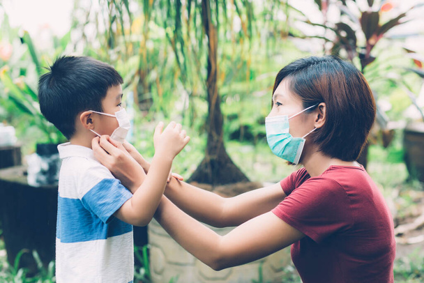 Μητέρα αναλάβει τη φροντίδα του γιου με μάσκα προσώπου για την προστασία της γρίπης της νόσου ή covid-19 σε εξωτερικούς χώρους, μαμά φορώντας ιατρική μάσκα με ασφάλεια των παιδιών για την προστασία ξέσπασμα πανδημίας στο κοινό, ιατρική έννοια. - Φωτογραφία, εικόνα