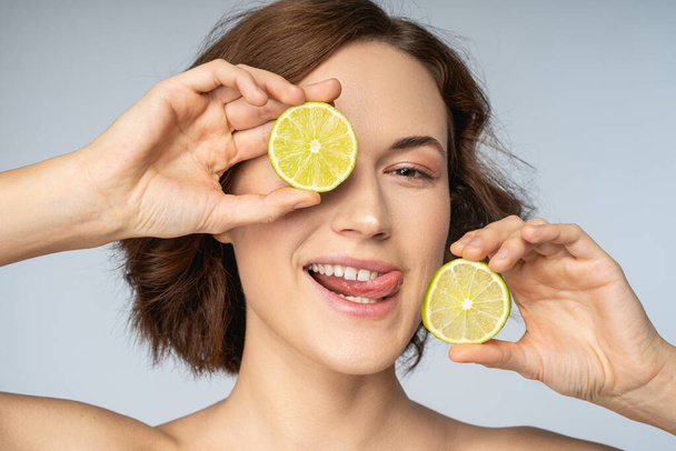 Jolly young woman holding half of lime around face - Φωτογραφία, εικόνα