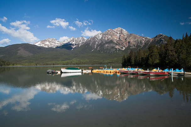 Wonderful reflections on blue water of Pyramid Lake, Jasper National Park, Alberta, Canada, with tourists boats on a little pier  - Photo, Image