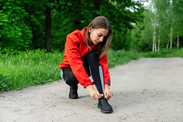 young girl tying shoelaces before running on a summer forest trail - Photo, Image