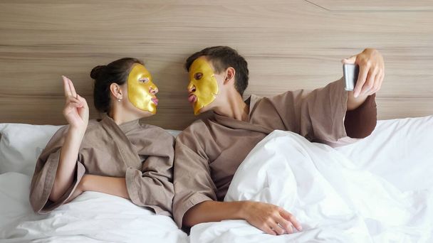 rodzina z maskami sprawia, że selfie w miękkim łóżku w hotelu - Zdjęcie, obraz