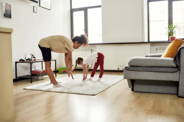A better way to practice care. African american woman baby sitter and caucasian cute little girl having workout at home. Children education, leisure activities, babysitting concept - Foto, Imagem