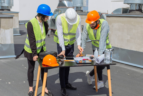 Multiethnic group of workers engineers architects foreman analyzing the plan of construction site on the rooftop of modern building - Photo, Image