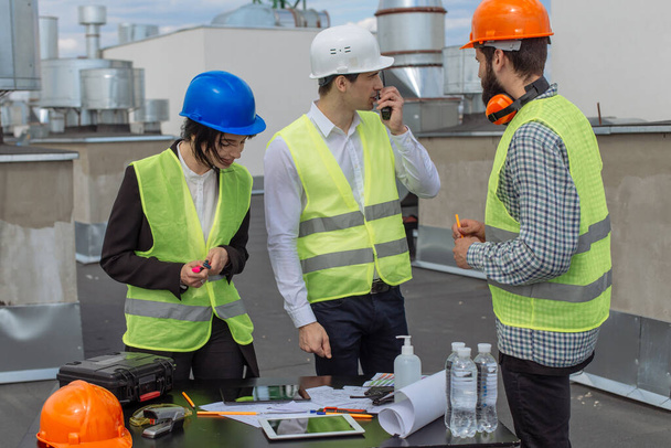 Мультиэтническая группа рабочих архитектор и два инженера беседуют на крыше здания анализируя стройплощадку и разговаривая через рацион с другими рабочими
 - Фото, изображение