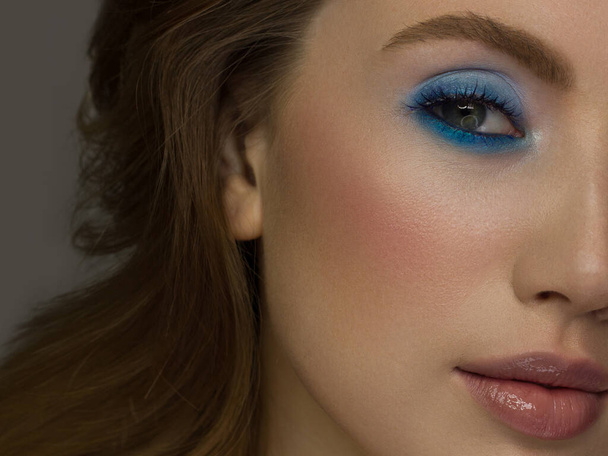 Half a beauty portrait with beautiful fashionable evening make-up, black jiggles on eyes and extremely long eyelashes. Natural lipstick on the lips and blue eyehadow. Cosmetology and facial skin care - 写真・画像
