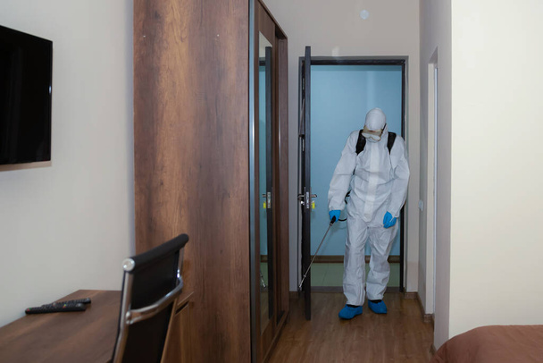 Pessoas em trajes de proteção de vírus e máscara desinfetando edifícios de coronavírus com o pulverizador
 - Foto, Imagem