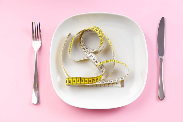 Стрічка вимірювання втрати ваги на білій тарілці, концепція здорового харчування. рожевий фон
. - Фото, зображення