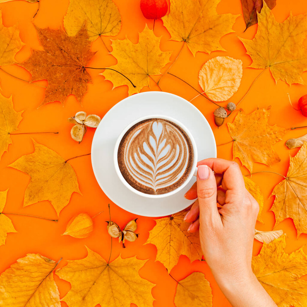 Podzimní plochá kompozice se suchými listy věnec rám a káva latte šálek v ruce ženy na tučném oranžové barvy pozadí. Kreativní podzimní díkůvzdání, podzim, halloween koncept. Horní pohled, kopírovací prostor - Fotografie, Obrázek