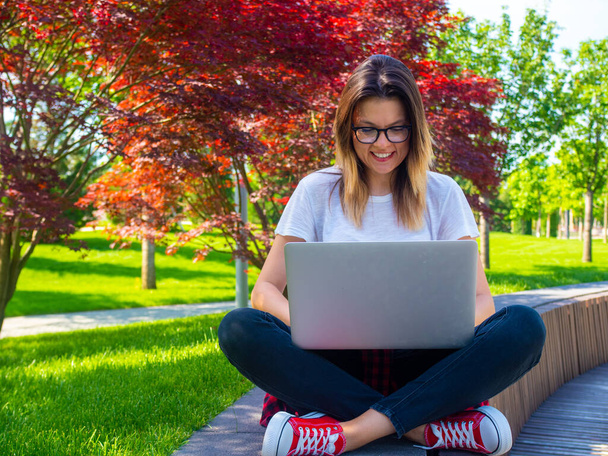 女性のクロス座って、ラップトップの屋外で足。オンライン教育の概念 - 写真・画像
