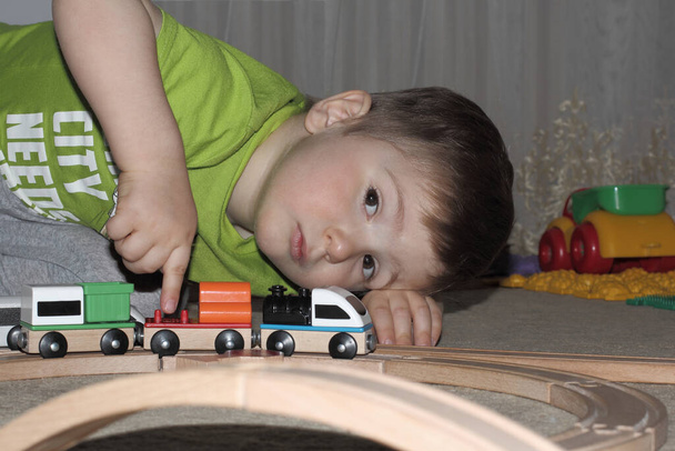 un petit garçon est assis sur le sol dans une chambre d'enfants et joue avec un chemin de fer jouet. Finger pousse un train de jouets sur des rails en bois. - Photo, image