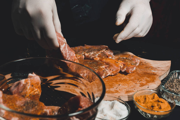 Marinoin raakaa sianlihaa kebabien ja kinkun keittämiseen. Ravintolan käsineiden keittiömestari käsittelee lihaa basilikan ja curryn mausteilla 2021. - Valokuva, kuva